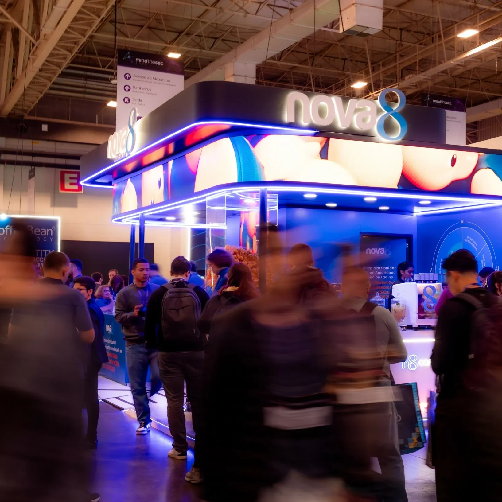 Estande da Nova8 iluminado em azul no evento Mind The Sec 2026, com visitantes circulando em frente