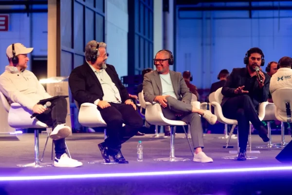 Quatro participantes com fones de ouvido sentados em palco durante painel de debate, um deles falando ao microfone